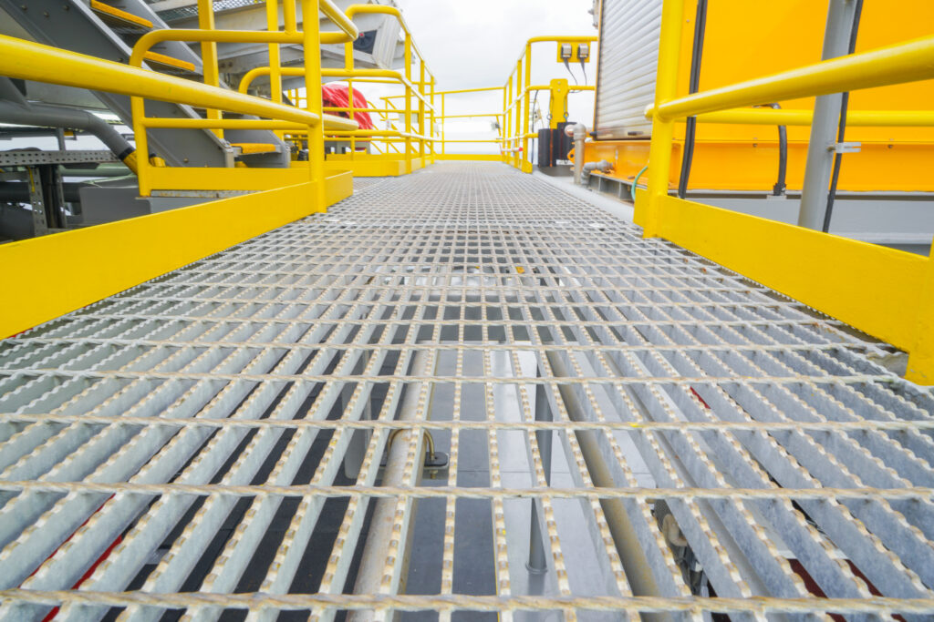 Galvanised steel walkway mesh with bright yellow handrails inside of a industrial warehouse